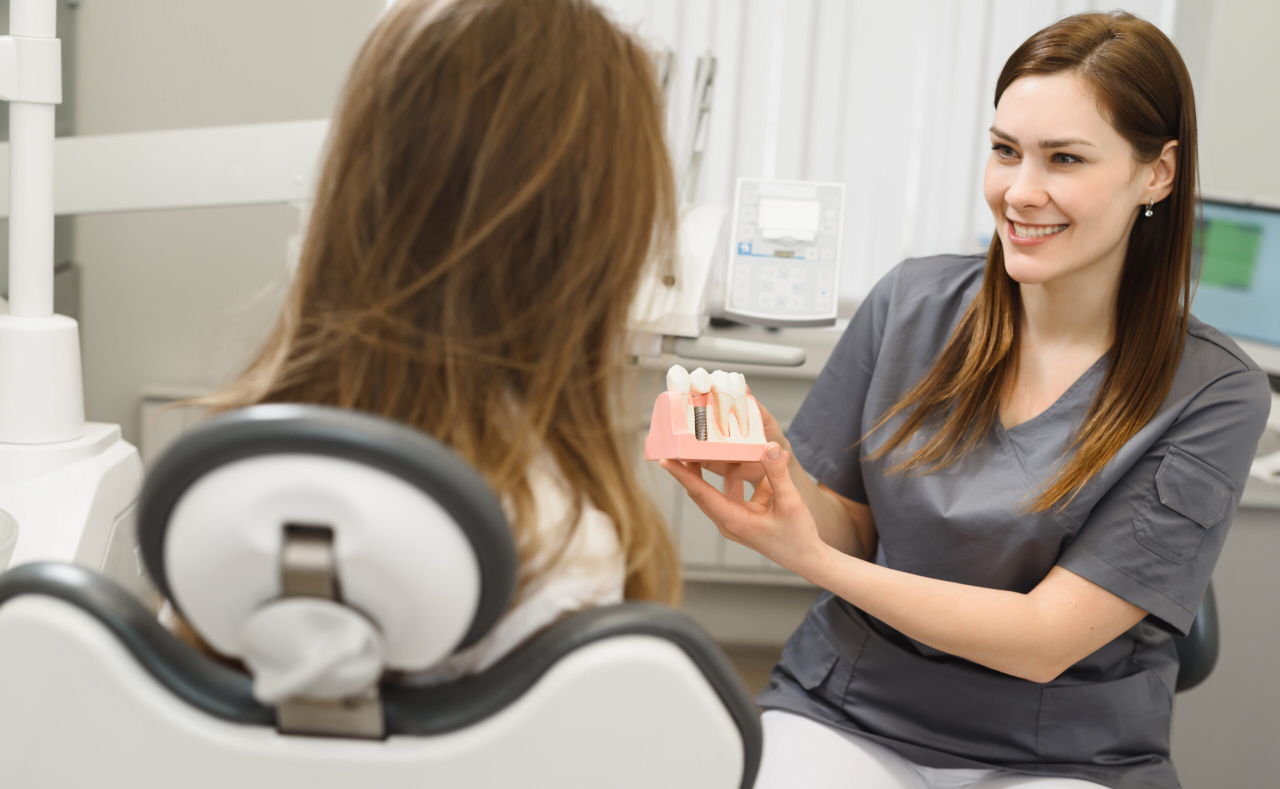 Dental assistant showing a patient a model of a dental implant