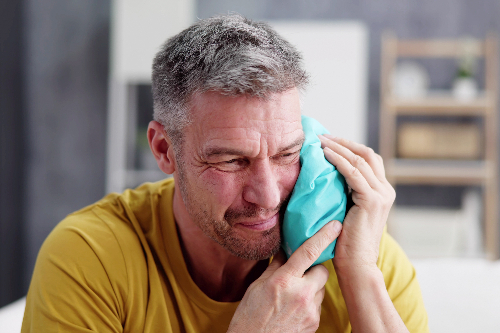 man suffering from severe tooth pain holding a ice pack on jaw