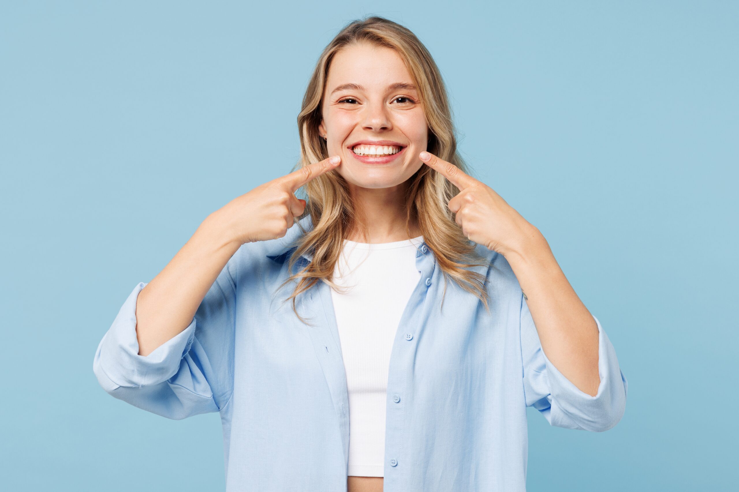 young woman against a blue background showing off her white smile