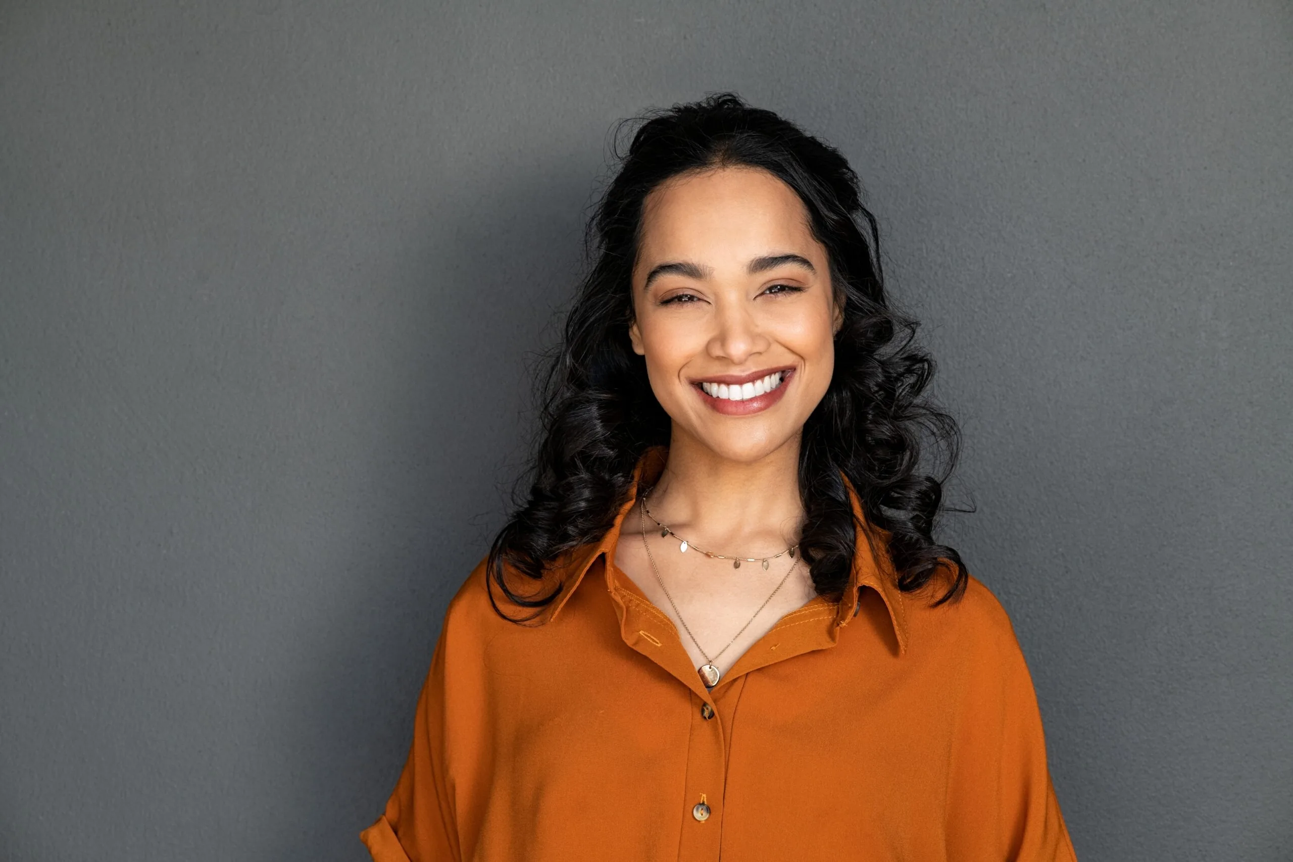 young woman showing her new dental veneers against a grey background