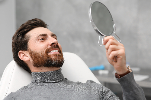man smiling in a mirror sitting in a dental office, new dental implants