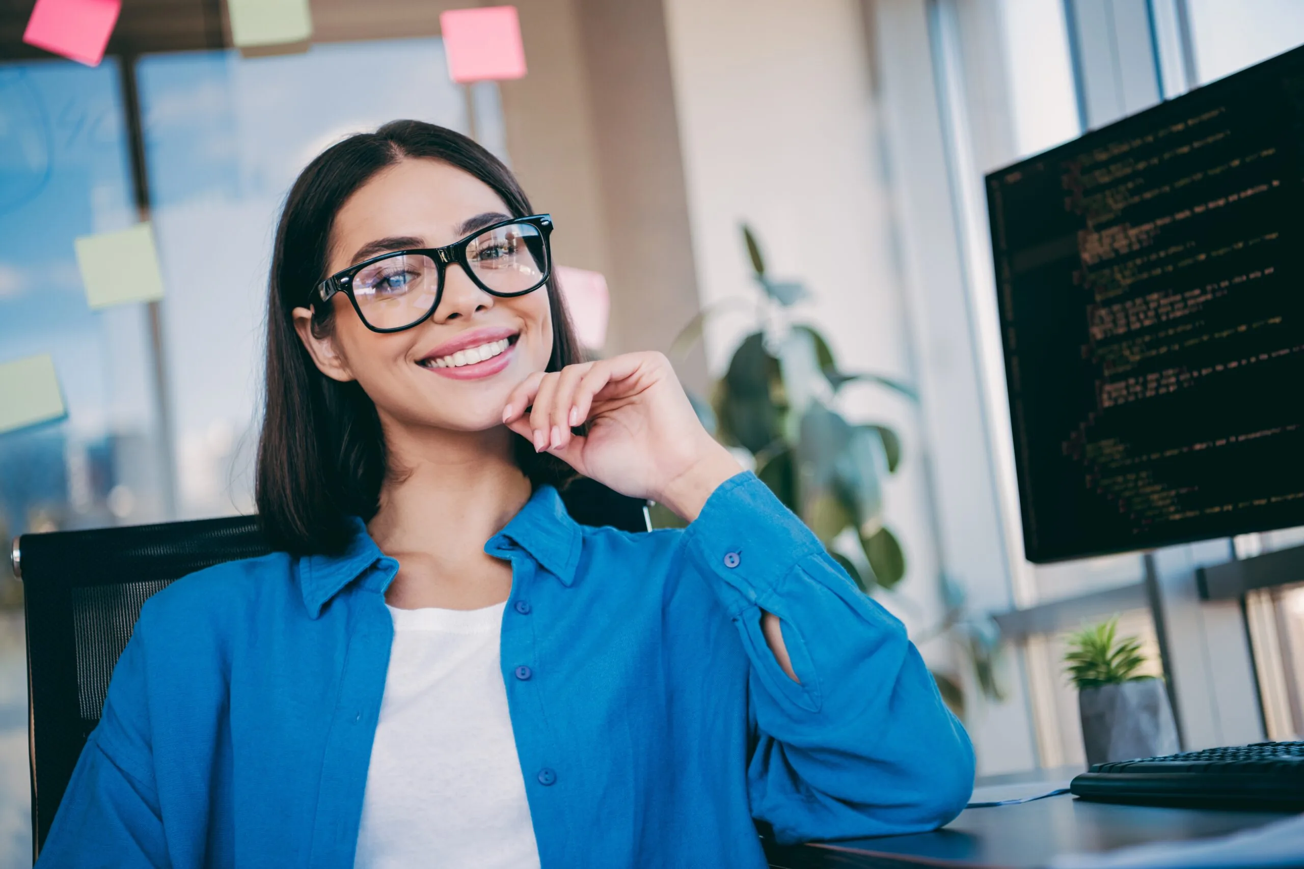 A confident businesswoman sits at a clean desk in a bright loft office, smiling, perfect white teeth