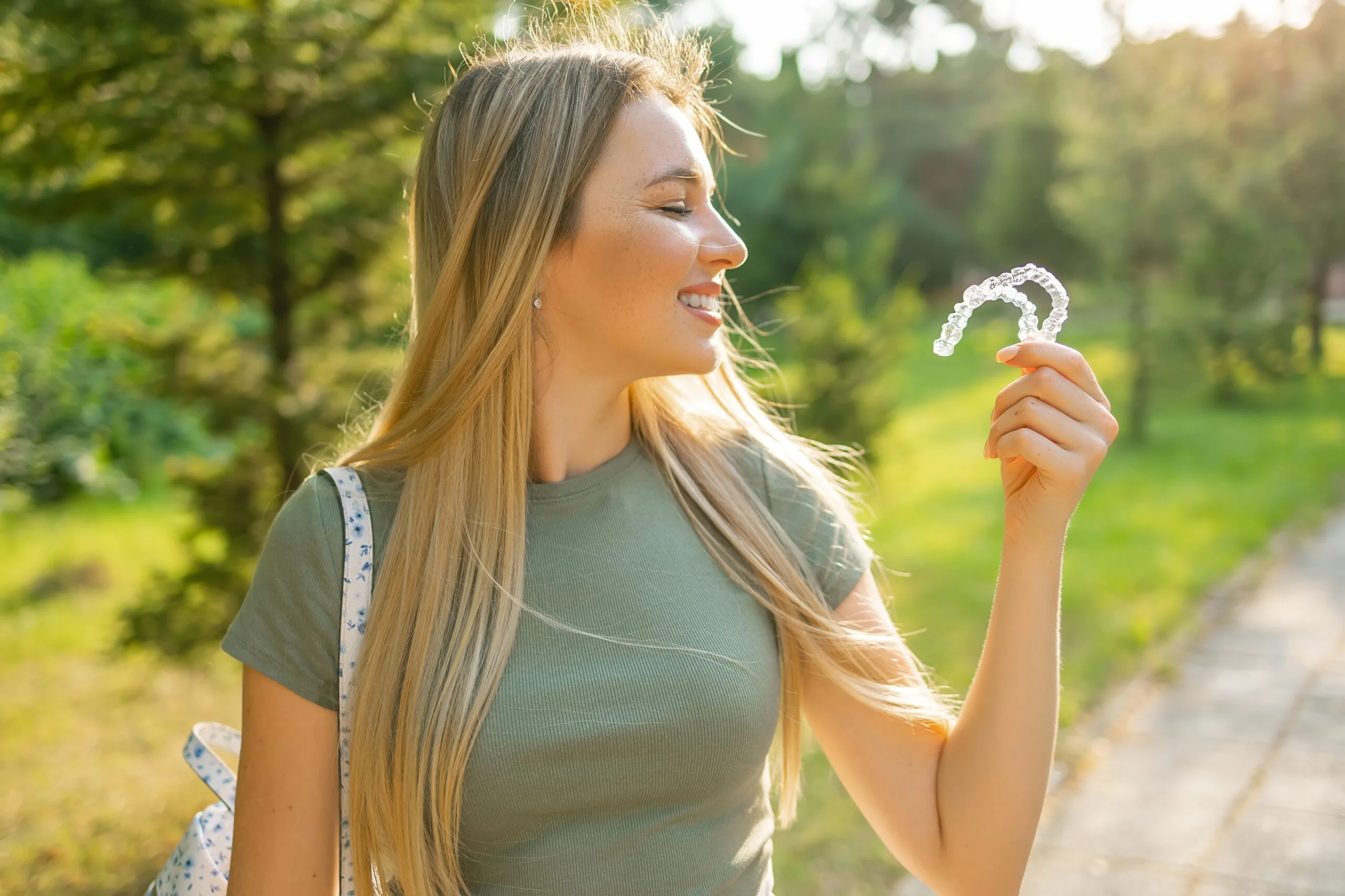 side view of a woman with clear aligners in hand, outdoors