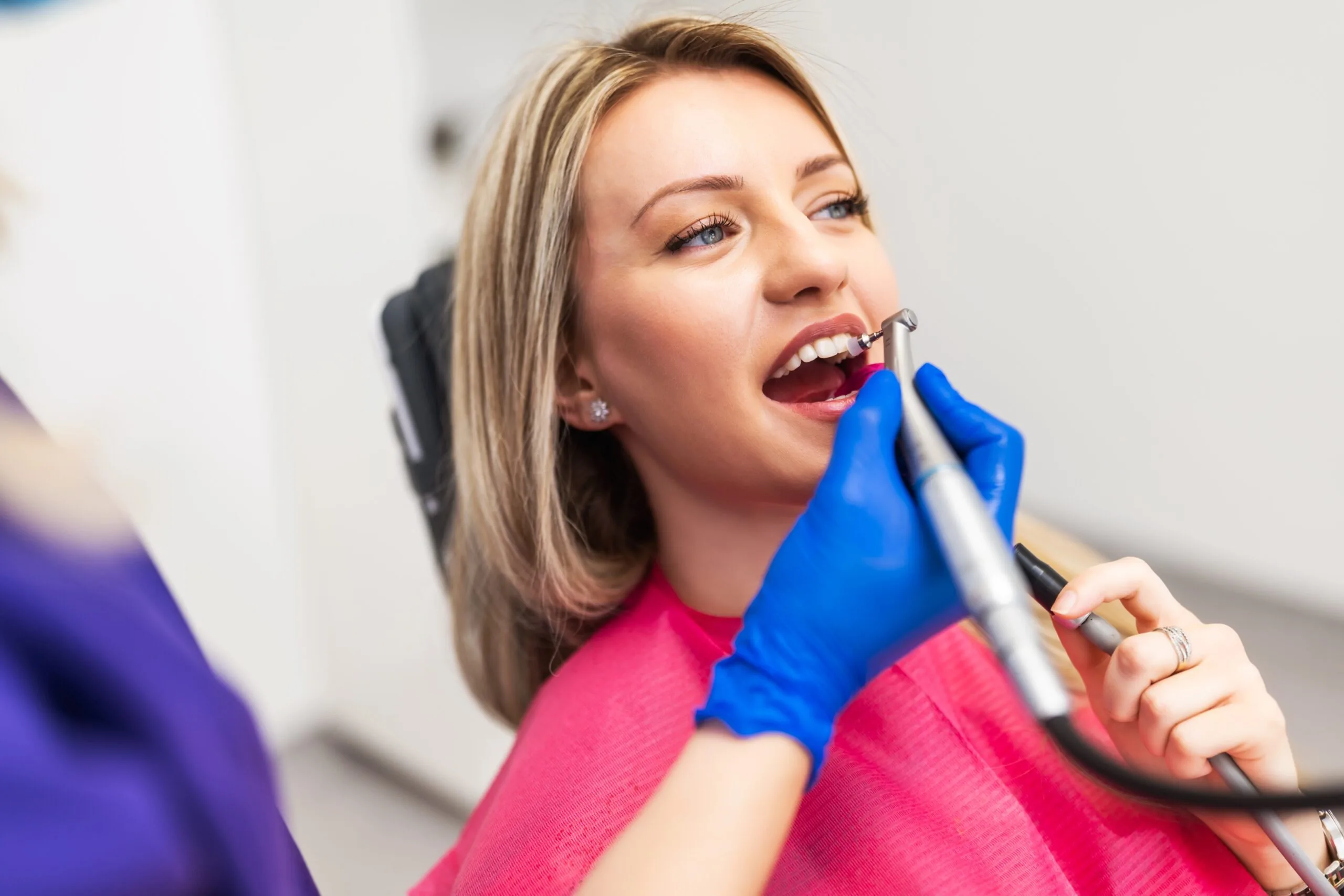 dentist in blue gloves polishing a female patients dental crown